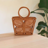 The Butterfly Rattan Handbag handmade by Ganapati Crafts Co. in Bali is sitting on a table looking stylish